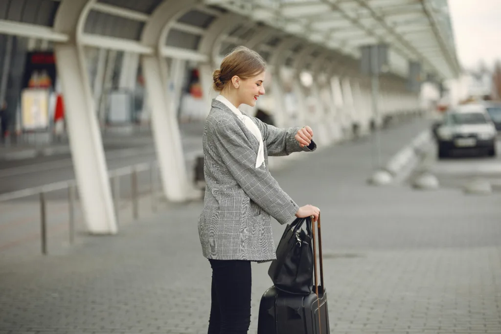 Woman in gray jacket checking wristwatch at station with luggage, representing punctual travel.