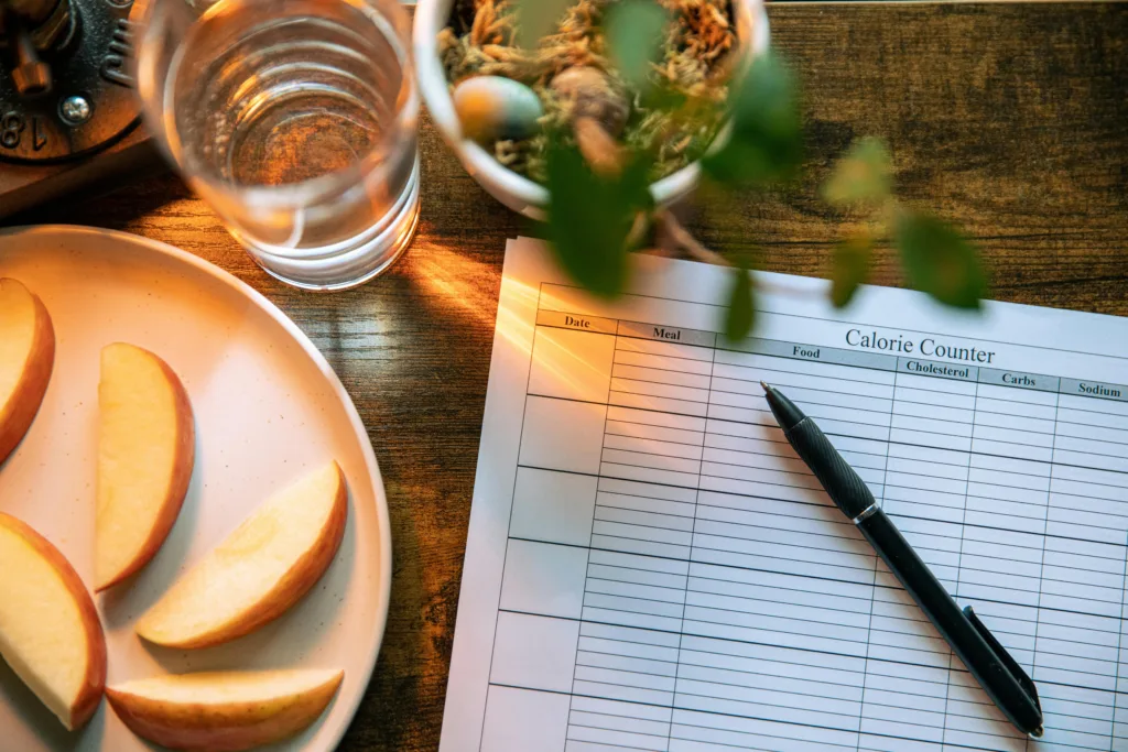 Apple slices, water glass, and a pen on a calorie counter sheet - a healthy lifestyle concept.