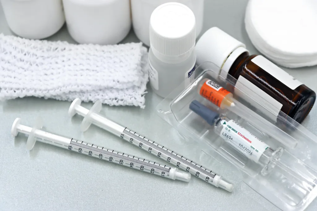 Flat lay of medical tools and vaccines, including syringes and bottles, on a white surface.