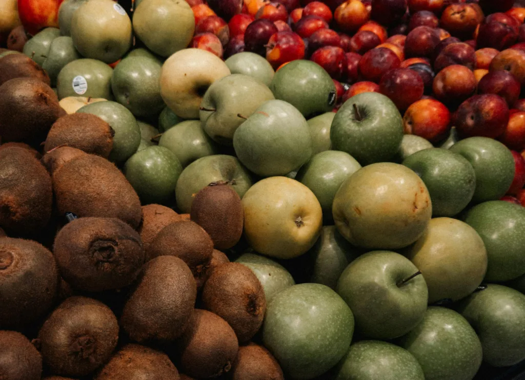 A vibrant display of apples, kiwis, and plums at a market stall, showcasing fresh produce.