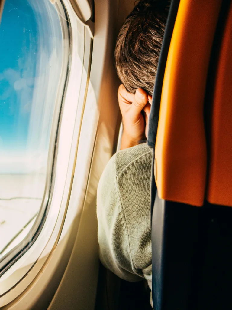 A man resting by the airplane window, peering into the sky during a daytime flight.