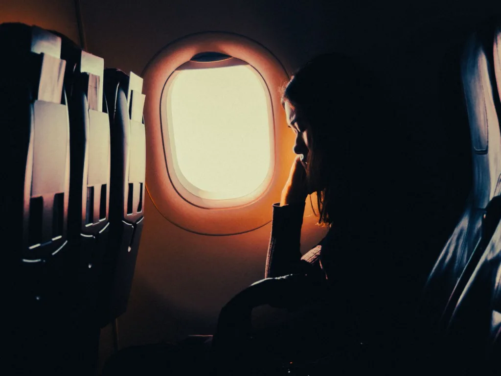 Silhouette of a woman resting by a window seat on an airplane, offering a serene travel moment.